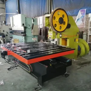 Industrial metalworking machine with a large yellow gear and orange-framed table in a factory.