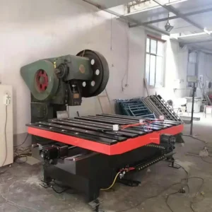Large green industrial press with a circular flywheel beside a red slat-bed worktable in a workshop