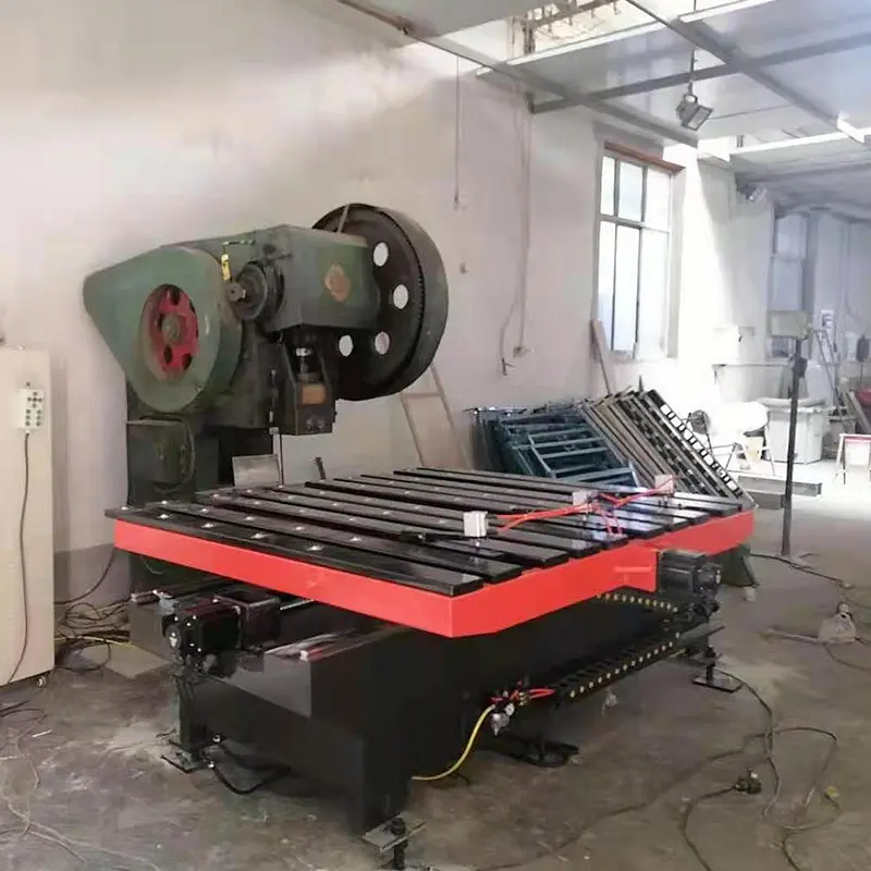 Large green industrial press with a circular flywheel beside a red slat-bed worktable in a workshop